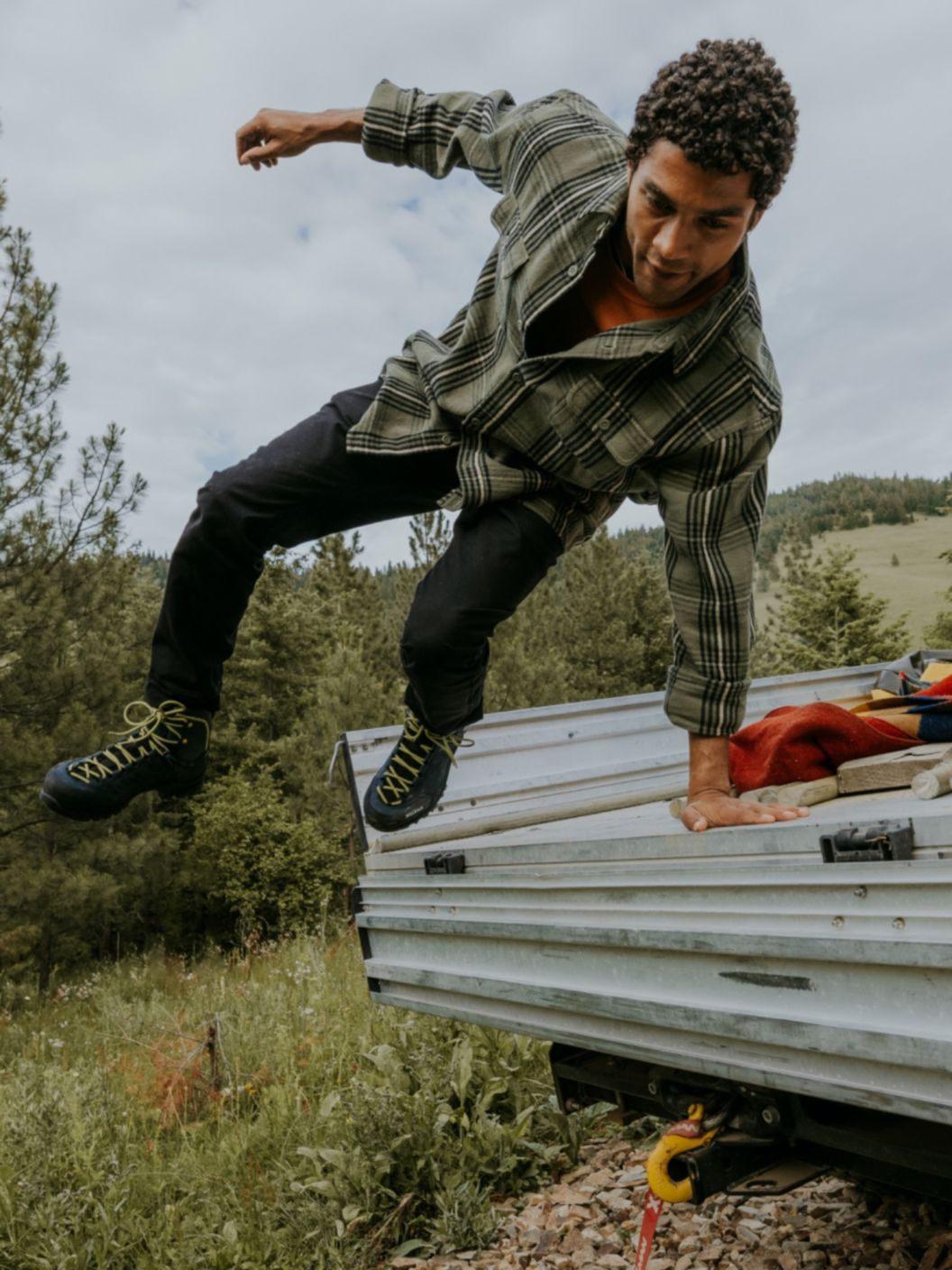 A man wearing a green flannel is in mid-air after jumping off the bed of a truck.